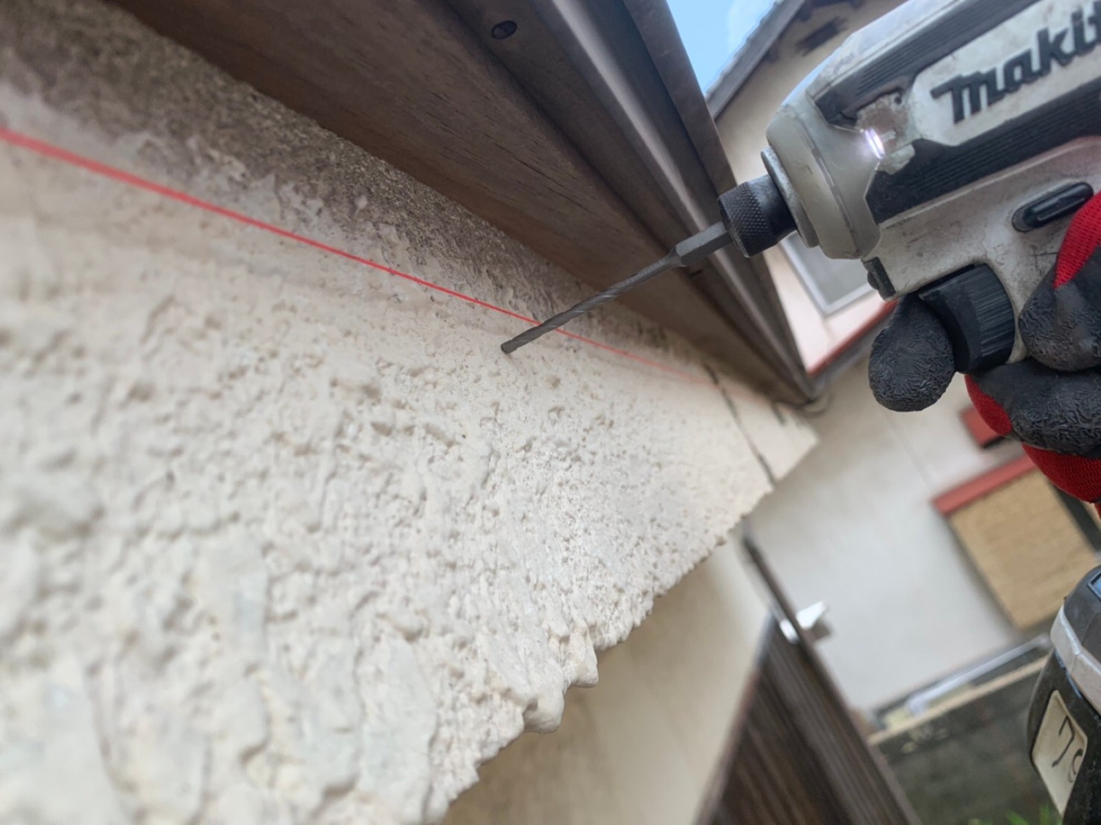 赤い水糸に合わせて電動工具で下穴をあける職人