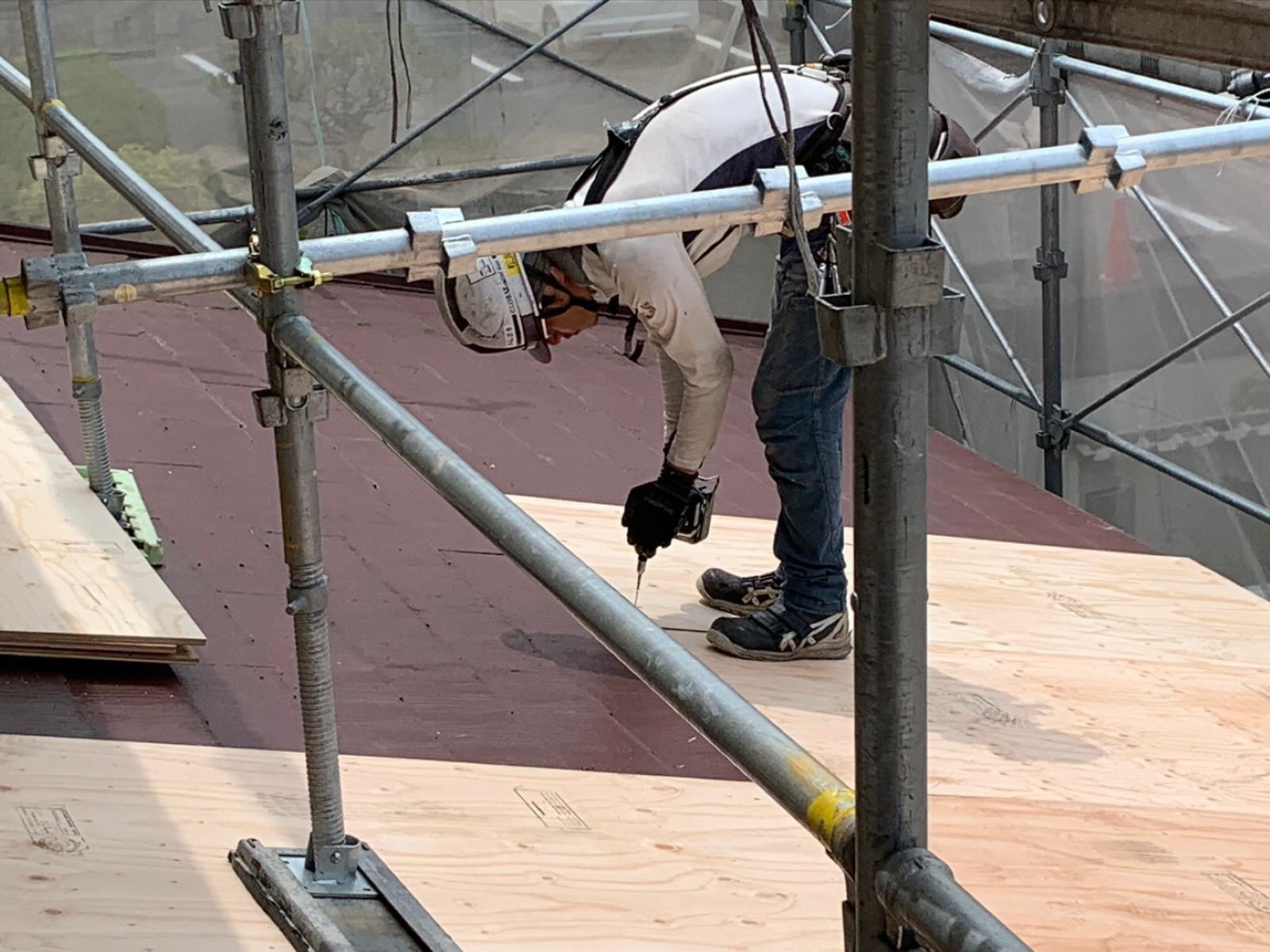 2階の屋根で合板を留め付ける職人