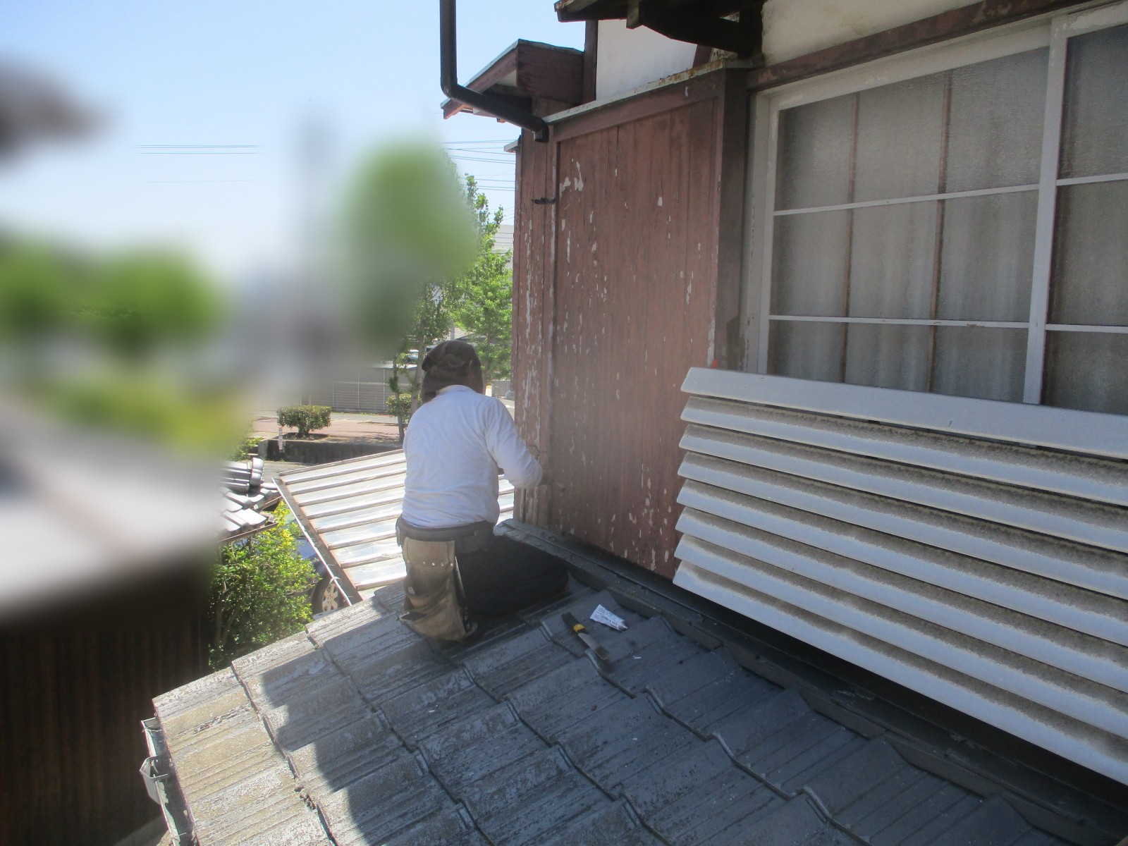 一段低い屋根の上で縦の樋を壁に取り付ける職人