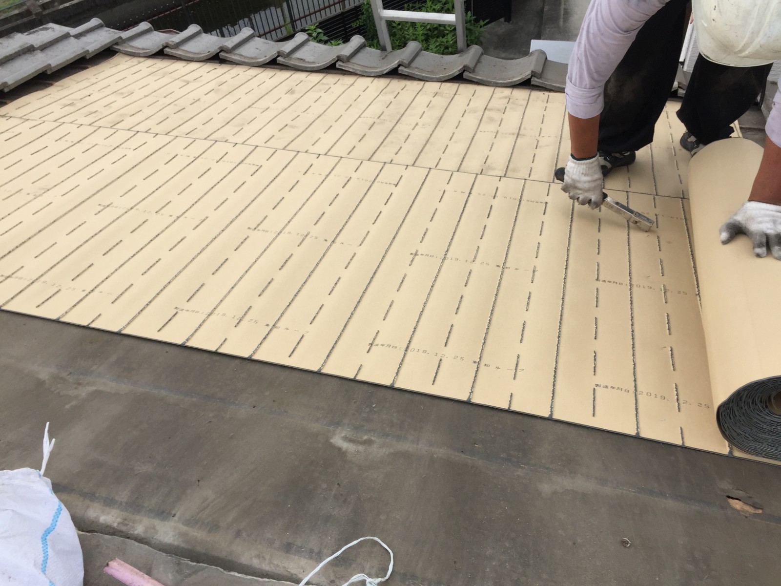 古い防水紙の上に新しい防水紙を張っていく職人