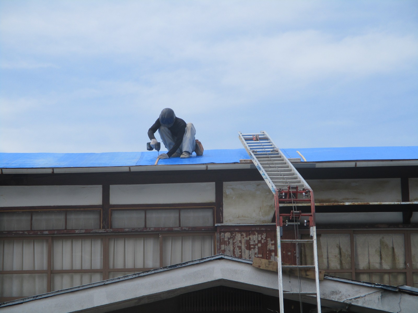 瓦を下ろした屋根をブルーシートで覆う職人