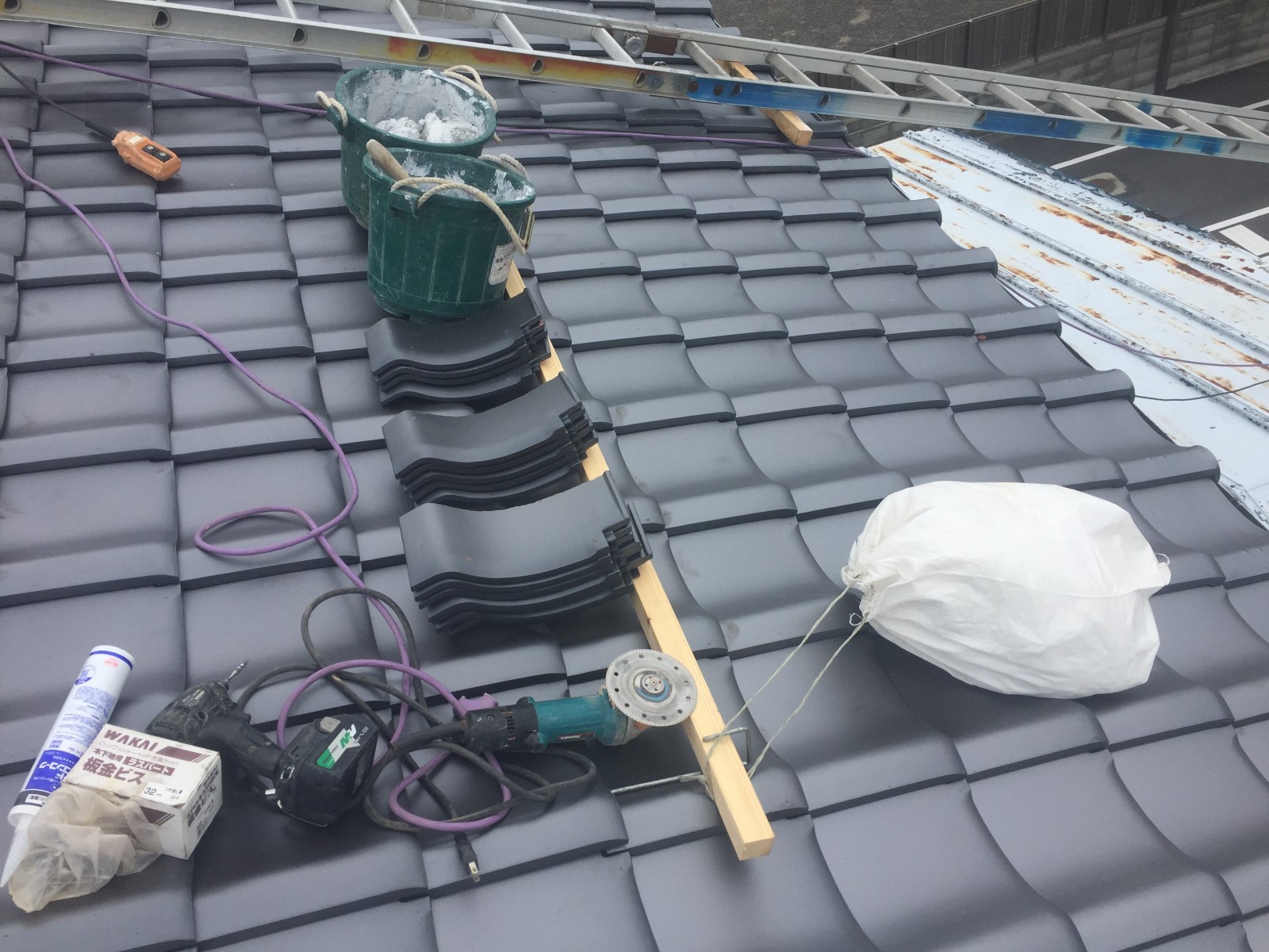 屋根の上に重ねた棟の丸い瓦とビスや電動の工具