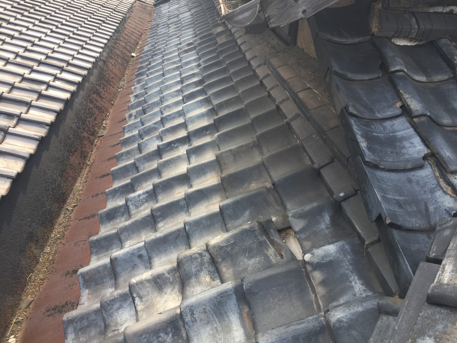 赤く錆びた谷板金と並びが乱れた谷ぞいの瓦