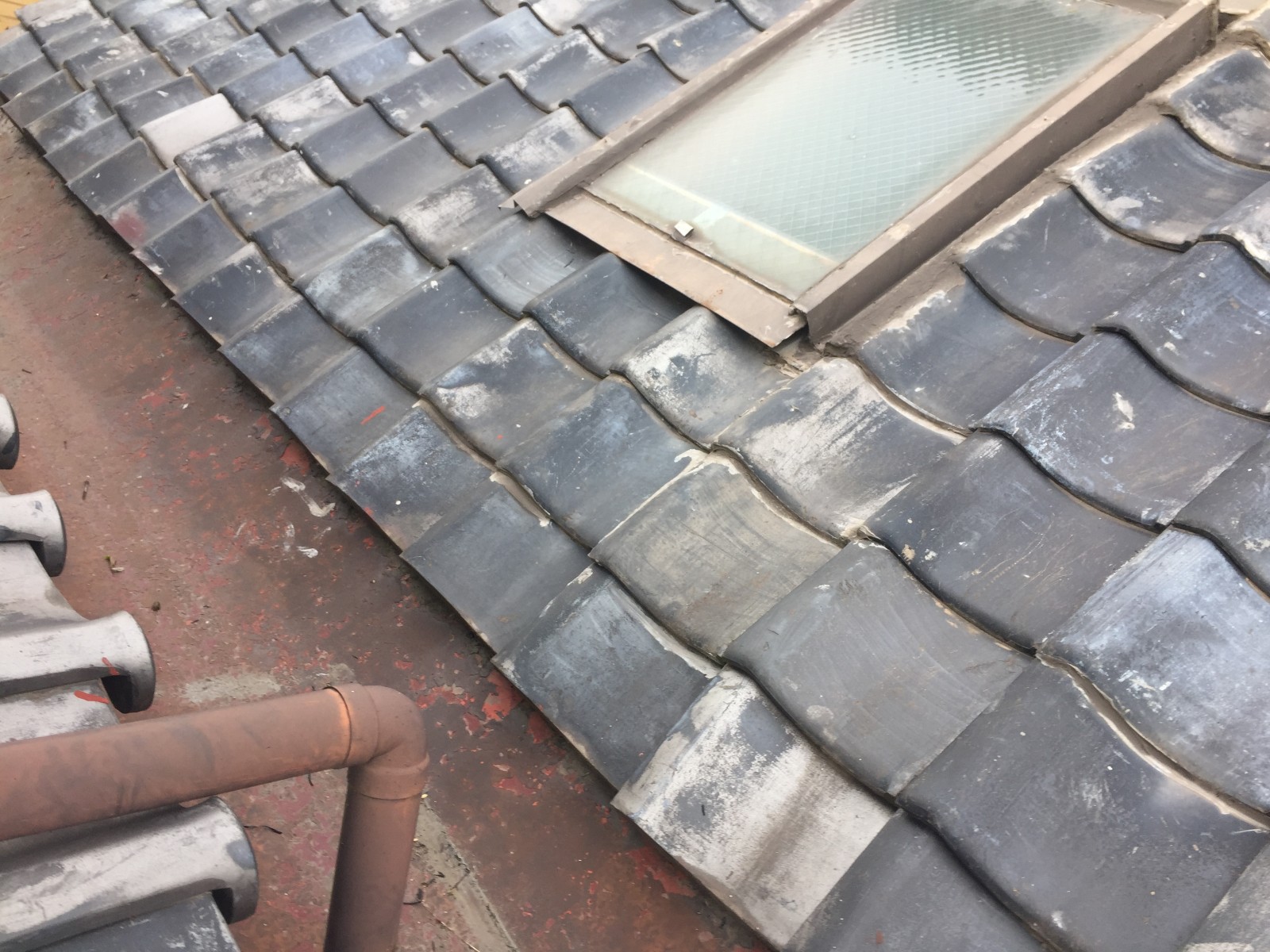 赤く錆びた板金と屋根の上を通る竪樋