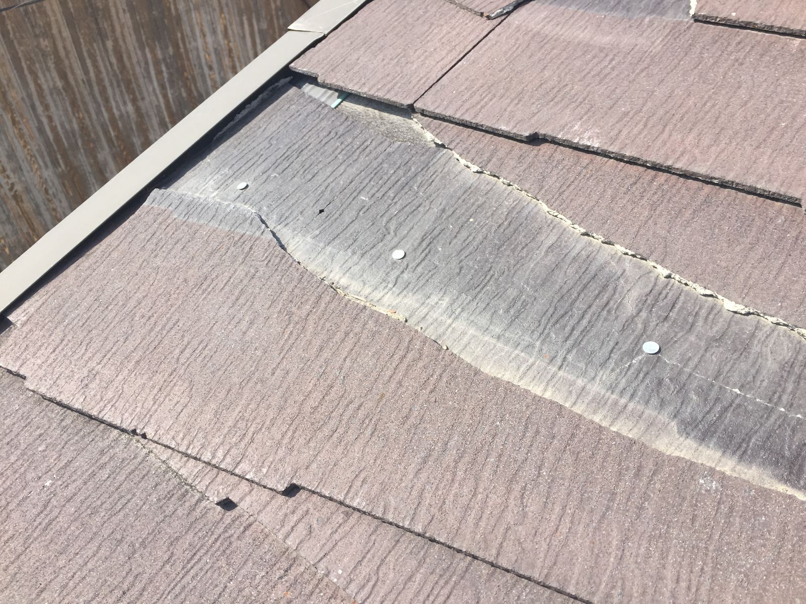 割れて一部がはがれ落ち、下地や留め釘が露出してしまっているスレート屋根