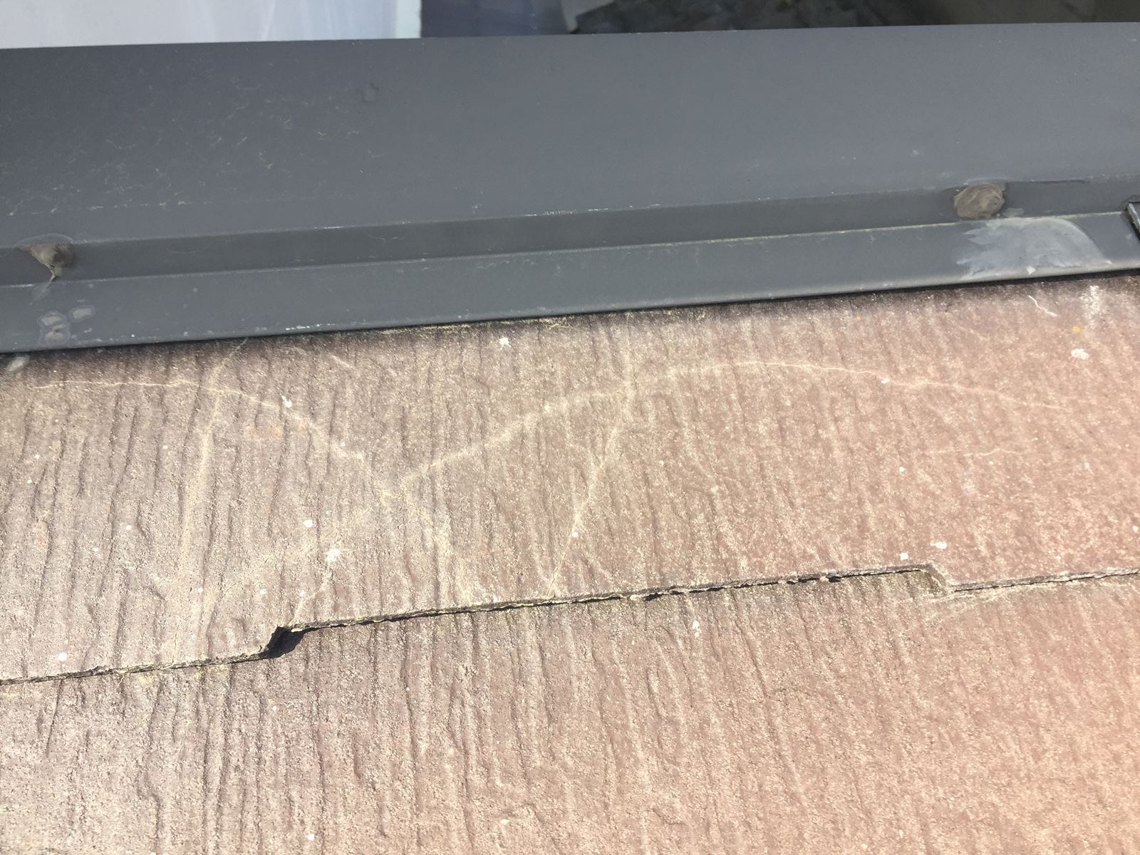 屋根の広範囲にわたって見られるスレート材の欠損と水分の染み込み